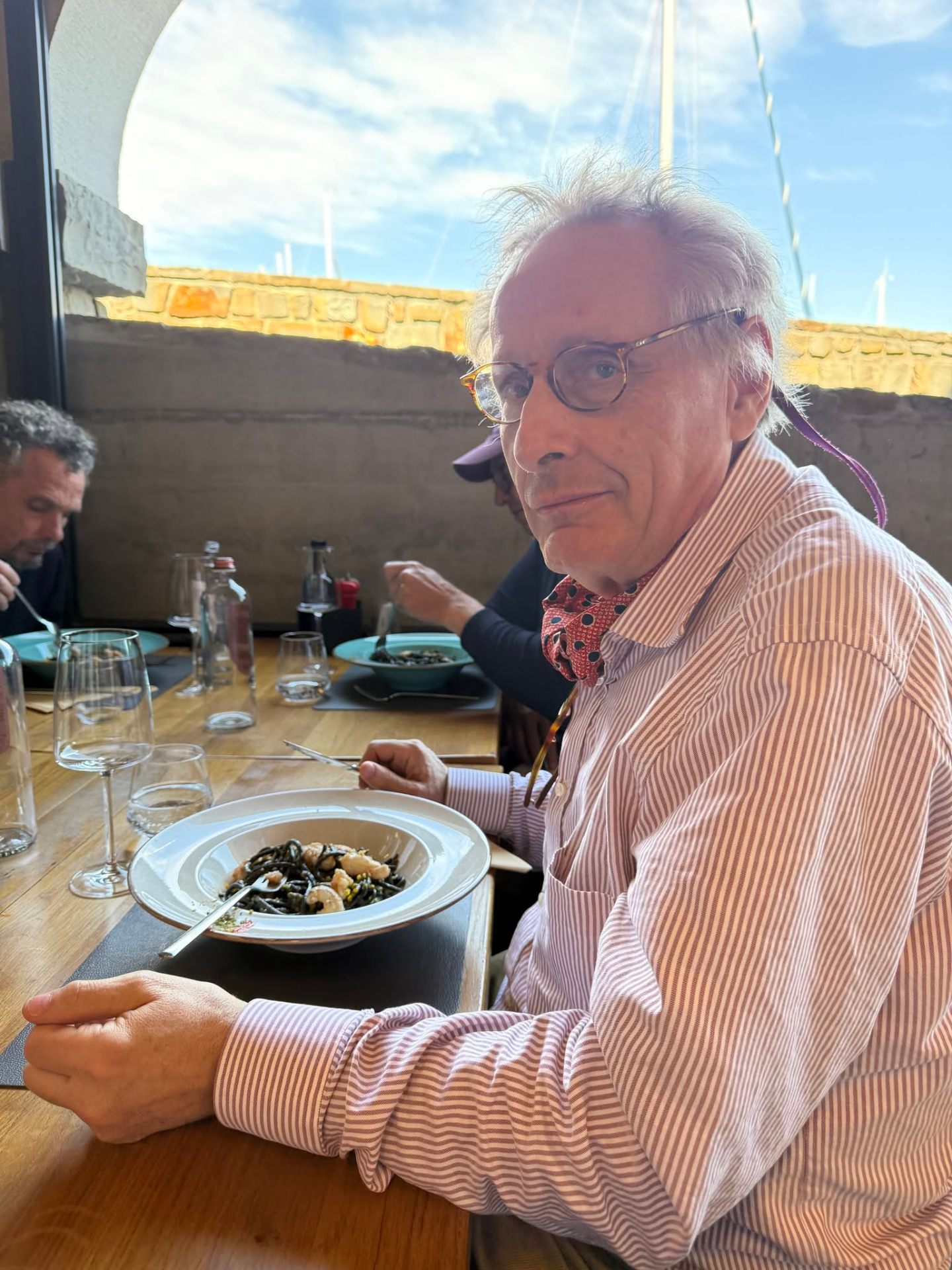Pierre enjoying squid-ink pasta at a Mediterranean waterfront restaurant.
