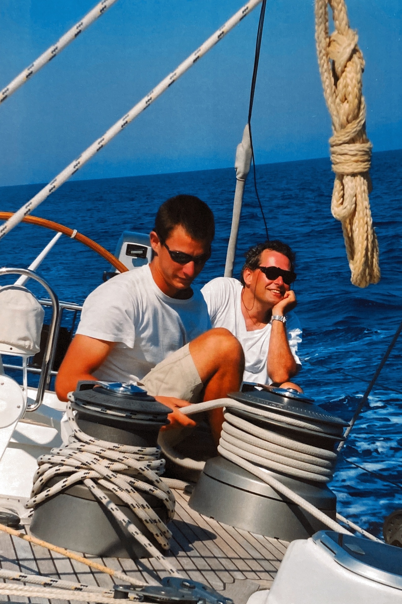 A young Pierre relaxing on a sailboat with a friend under a bright blue sky.